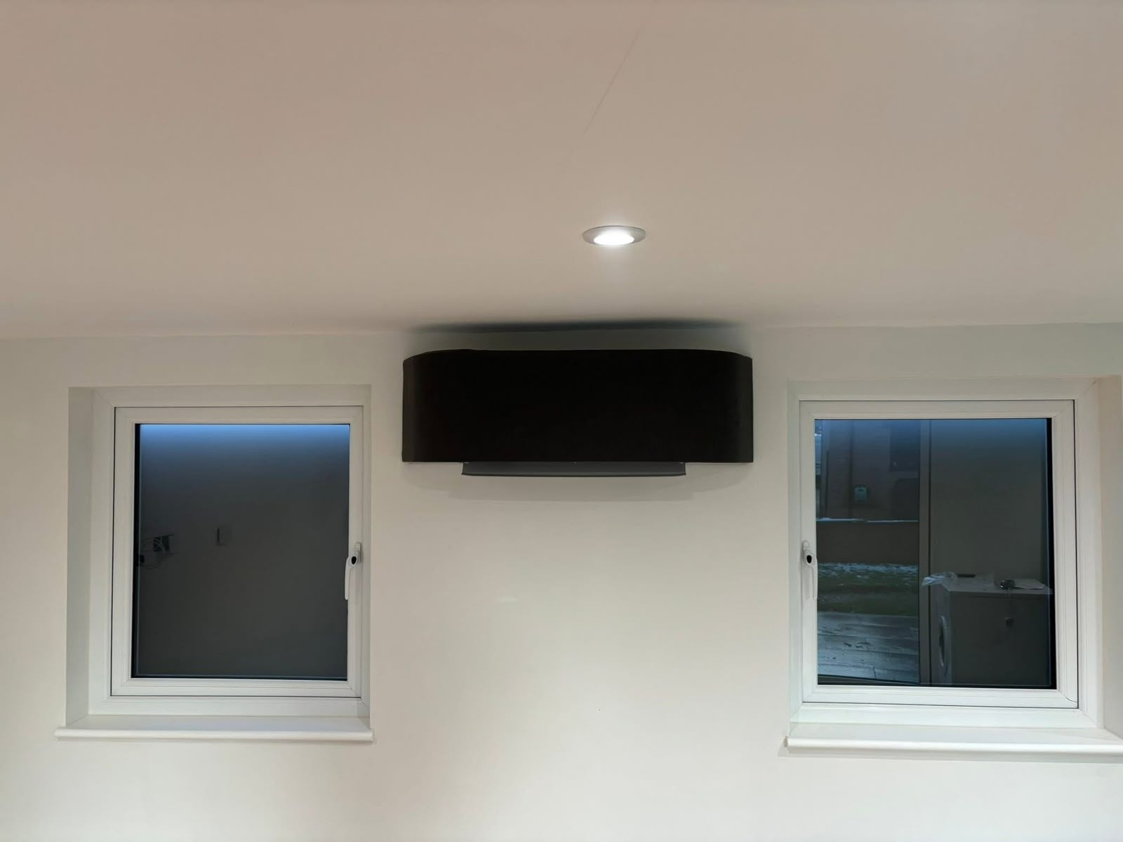Black low-wall air conditioning unit fitted between two windows in a home