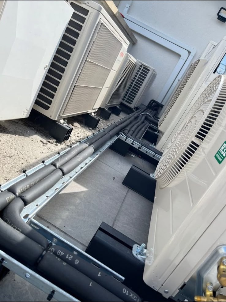 Multiple outdoor condenser units set out with neatly routed refrigerant pipework after a designed system install